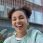 Happy optimistic girl with two hair buns dressed in jacket enjoys free time and walking in city holds bottle of detox drink makes selfie poses against modern building has fun during daytime.